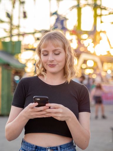 A vertical shot of a young blonde female using her phone at an amusement park