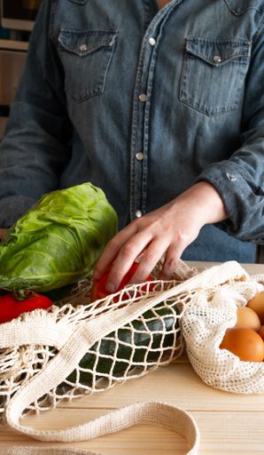 A vertical shot of a woman picking up sustainably made shopping with cardboard and cloth bag