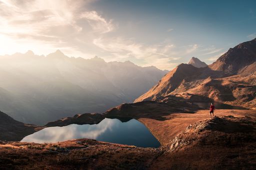 Landscape autumnal view of the Lacs de Fenetre with a hiker contemplating the sun setting behind the mountains