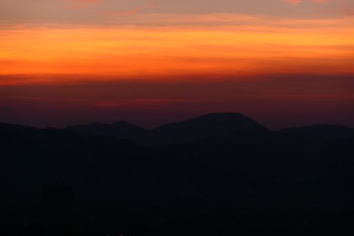 A vibrant orange sky illuminated by a setting sun  framed by majestic mountain peaks in the distance