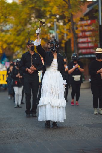 A climate activist in a white dress and a gas mask rings a bell while leading protesters in demonstration against oil and gas during the Fall season.