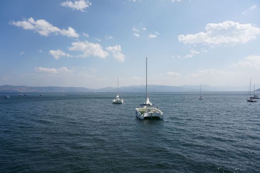 A scenic view of multiple sailboats in the distant horizon, with picturesque mountains and clouds in the background