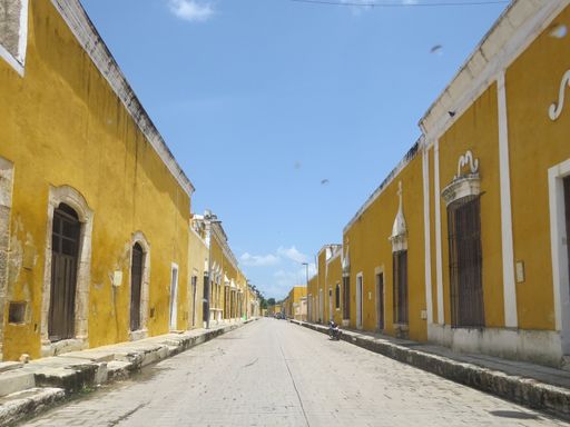 An idyllic street scene featuring rows of sunny yellow buildings with white accents, creating a cheerful atmosphere in the empty street