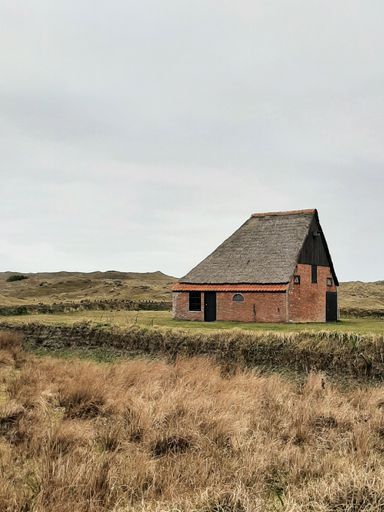 A traditional red-colored building situated on the edge of a grassy field, with a clear blue sky in the background