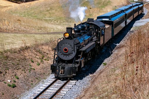 A Front and Slightly Above View of an Approaching Restored Narrow Gauge Passenger Steam Train Blowing Smoke and Steam on a Sunny Winter Day