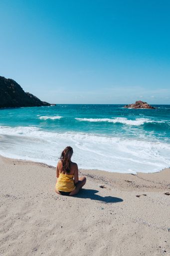 A vertical back view of a female sitting on a beach on a sunny day