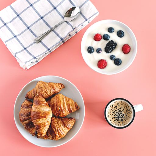 A top view of delicious croissants, hot coffee and yogurt with berries for breakfast