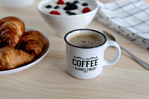 A closeup shot of a cup of breakfast coffee and a croissant