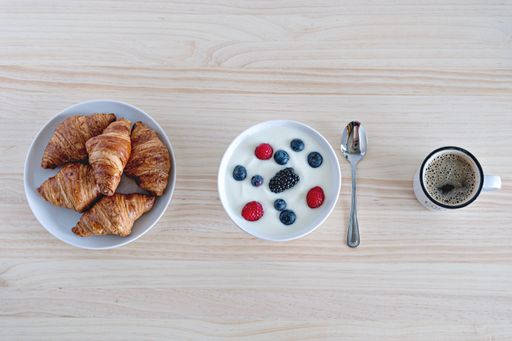 A top view of a breakfast table with coffee, croissants, and a bowl of berries with yogurt