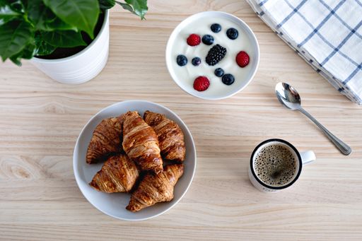 A top view of a breakfast table with coffee, croissants, and a bowl of berries with yogurt