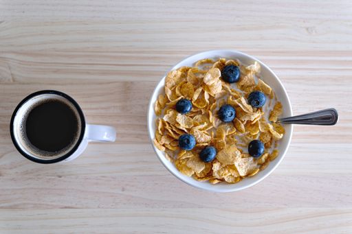 A top view of a bowl with delicious cereal and blueberries near a cup of coffee