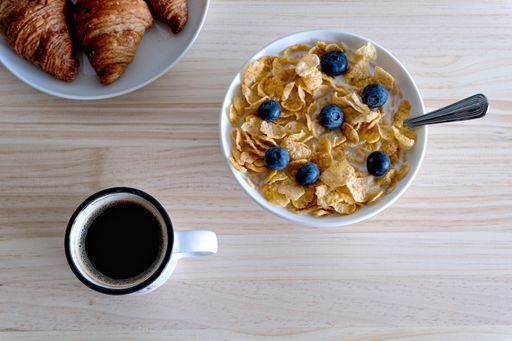 A top view of a bowl with delicious cereal and blueberries near a cup of coffee