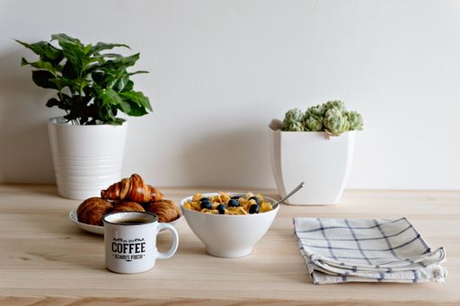 A breakfast table with coffee, croissants, and a bowl of berry cereal