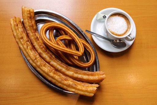 A high angle shot of a plate with churros and a cup of coffee