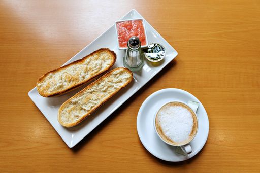 A top view of a cup of cappuccino with breakfast slices on a plate