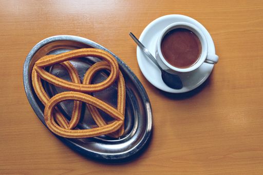 A high angle shot of a plate with churros and a cup of coffee