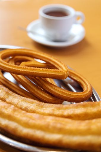 A vertical closeup shot of a plate with churros and a cup of coffee