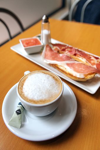 A vertical closeup shot of a cup of cappuccino with bread and ham