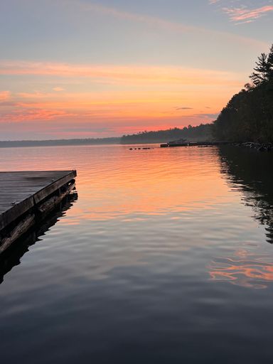 A wooden pier extends out over a tranquil lake surrounded by a vibrant sunset sky