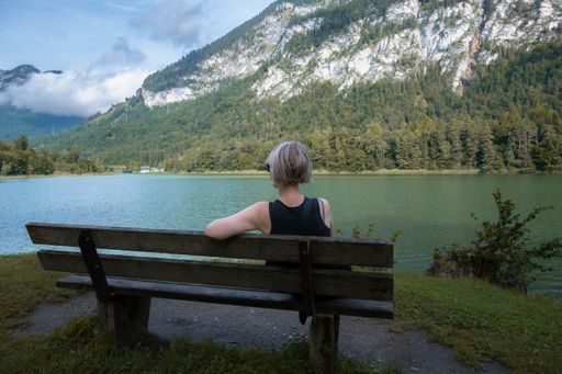 A rear view of a female seated on a bench in a park near a lake in the Tyrolean Alps