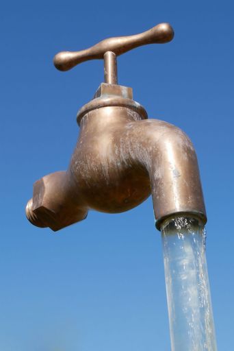 An aged metal tap releasing a steady stream of water against a beautiful bright blue sky