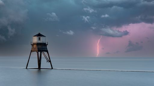 A dramatic view of a lighthouse silhouetted against a backdrop of lightning strikes