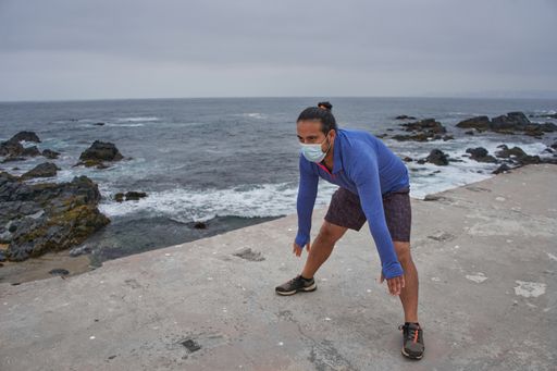 A man with a mask stretching in front of the sea - new normality, a sports session