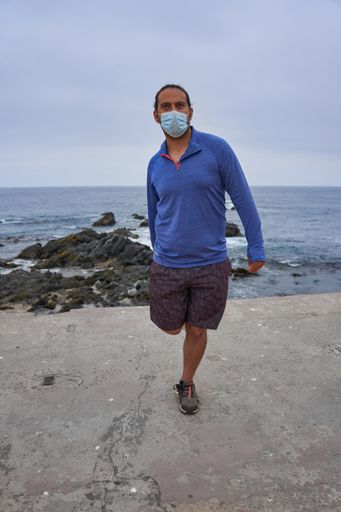 A man with a mask stretching in front of the sea - new normality, a sports session
