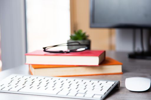 A computer desk with books, glasses, keyboard, and mouse on it