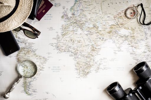 A top view of binoculars, a magnifying glass and a compass on a world map background
