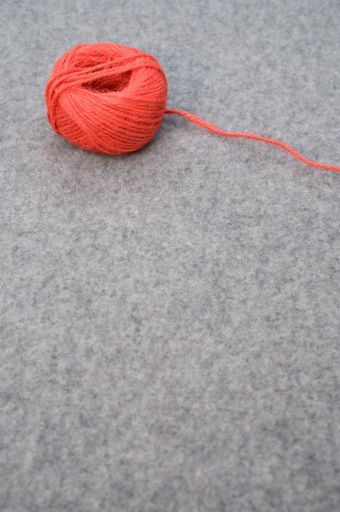 A vertical shot of a red ball of yarn with a loose string and copy text on gray background
