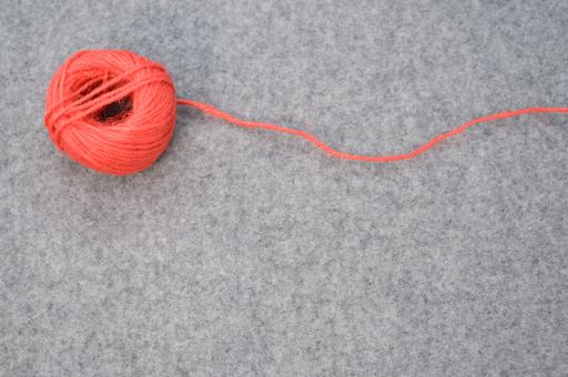 A red coil of yarn on a gray background with a loose string and copy space below