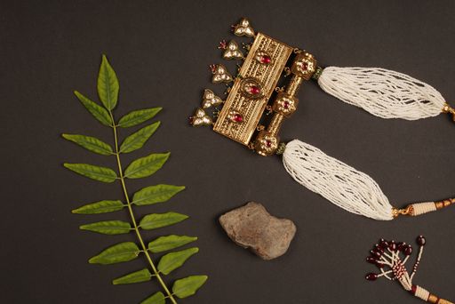 A top view of a beautiful necklace, a green leaf, and more on a dark surface