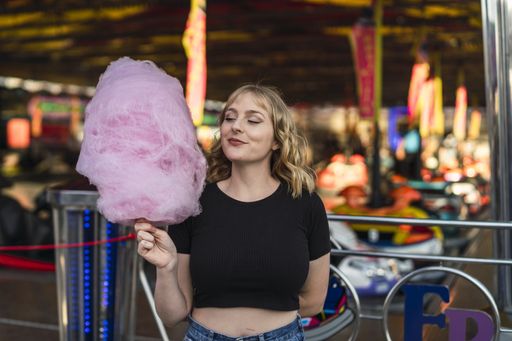 A blonde Spanish female eating cotton candy in an amusement park