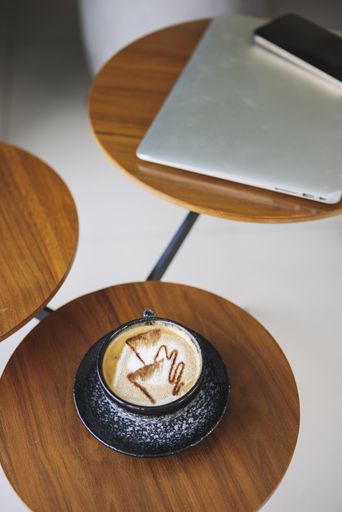 A vertical shot of a three-part round wooden table in a bright interior with a coffee on it in the foreground