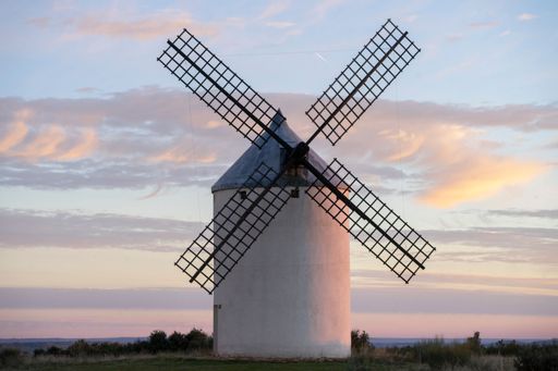 Lone windmill in the middle of the field at sunset with pink sky and clouds.