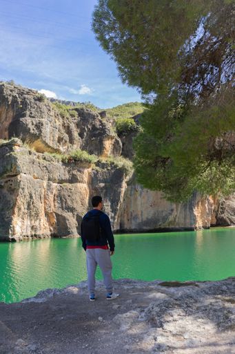 Young Caucasian person with sport clothes, enjoys nature looking at the mountains and a turquoise river. Absolute freedom. Healthy life in nature.