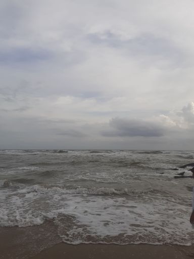 A solitary figure is walking along a sandy beach, with the expansive blue ocean visible in the distance