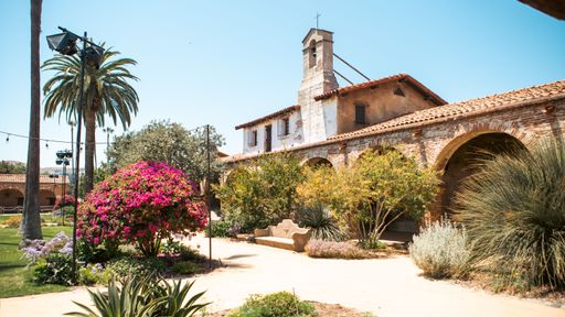 An array of colorful flowers in a well-maintained garden in front of a Creole-style building with a red-tiled roof