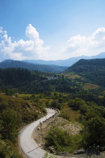 A vertical shot of a curving road in the wilderness around vast hills under a bright cloudy sky