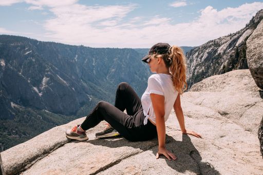 A young blond woman  sitting atop a rocky cliff in  in the Dolomites mountain range, California