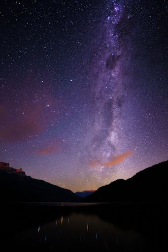 A breathtaking aerial view of a majestic mountain range with a lake below, illuminated by a beautiful milky way sky