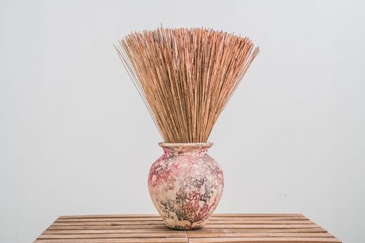 A vintage-style ceramic vase placed atop a wooden surface, displaying a natural straw plant