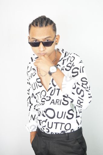 An Indian male in a fashionable shirt and sunglasses standing with a hand in his pocket