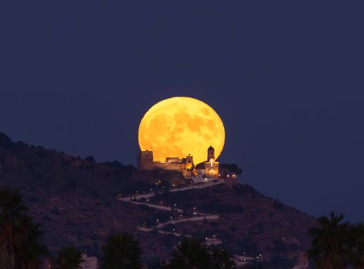 A scenic view of supermoon behind an old church on the hill at night