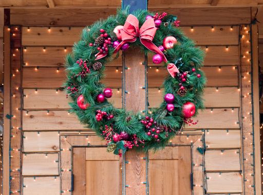A closeup shot of a Christmas wreath hanging on a wooden door decorated with string lights