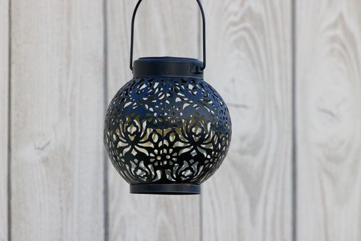 A closeup of a black ornate lantern against a wooden wall