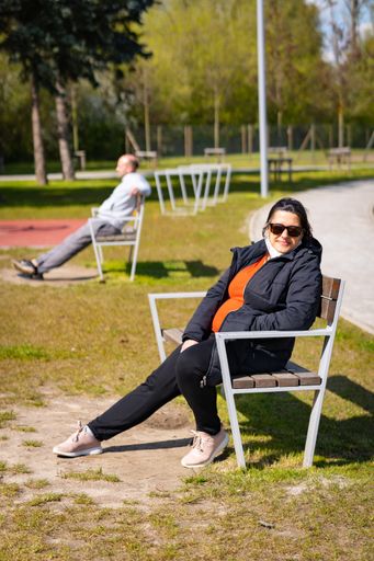 Woman with loose face mask sitting on a bench at a park in the city on a warm day in the spring season. One of the first sunny days.