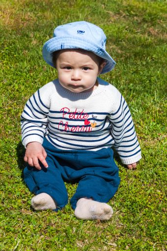 A vertical shot of a cute little Swiss baby boy sitting on green grass under sunlight