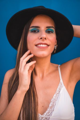 A beautiful brunette female in a black hat posing against a blue background